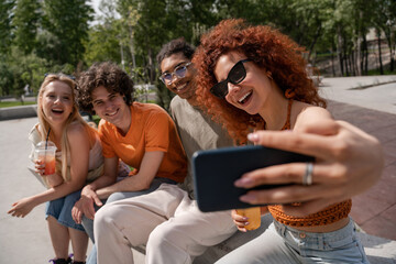 Obraz premium curly and cheerful woman in sunglasses taking selfie with multiethnic friends.