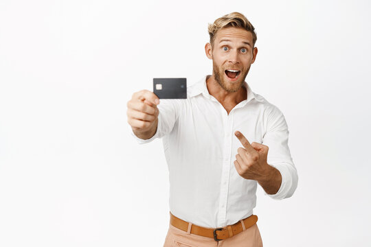 Image of smiling blond man showing credit card, banking product, standing against white background