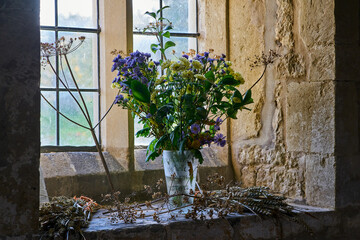 Beautiful vase of purple and yellow flowers sitting on church windowsill at harvest festival time