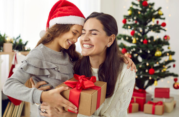 Fototapeta na wymiar Happy family sharing joy with each other on Christmas. Mother receives gifts from her loving child on Xmas Day. Smiling daughter gives present to mommy in living room with decorated tree in background