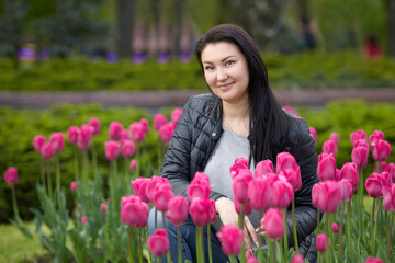 Beautiful young brunette sits in the park surrounded by tulips. High quality photo