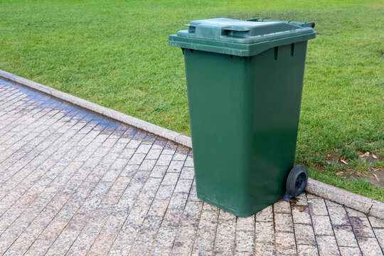 Plastic green garbage can for collecting garbage in the park. Mobile trash can with wheels