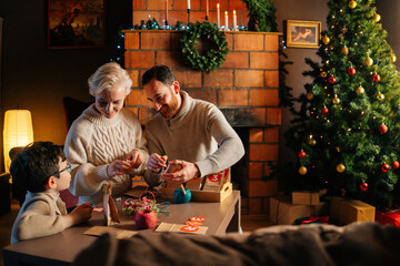 Cheerful young family making Christmas advent calendar together sitting at table on background of...