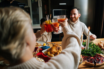 Close-up view from back to happy Caucasian family with adorable little child boy clinking glasses toasting at festive table during holiday family party, selective focus, blurred background.