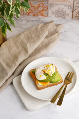 Savoury breakfast - A toast bread with cream cheese, avocado and poached egg on a white plate on marble tray