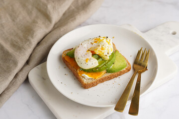 Savoury breakfast - A toast bread with cream cheese, avocado and poached egg on a white plate on marble tray