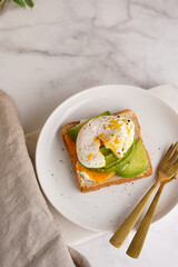 Savoury breakfast - A toast bread with cream cheese, avocado and poached egg on a white plate on marble tray