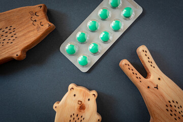 wooden toys cat, bear, rabbit and a blister of green pills on a black background. Children's...