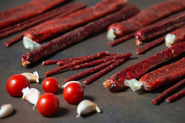 Thin appetizing spicy smoked sausages with different tastes and varieties of beef, pork, chicken, fish with tomatoes, spices and garlic on a dark background.