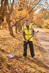 A man in a yellow vest raking leaves in the park