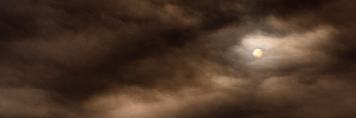mystical cloudy landscape. a wide view of the gloomy dramatic dark sky with thick cloudiness and dim sun behind atmospheric haze