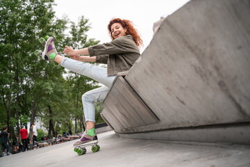 low angle view of cheerful woman tying laces on roller skate while sitting on border bench.