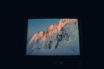 View of beautiful sunrise in mountains, seen through a window of a mountain hut or bivouac. High alpine mountain landscape with snow, ice and rocks. Mont Blanc Masiff, Chamonix, France.