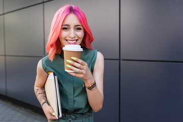 happy businesswoman with pink hair and earphone holding coffee to go and folders.