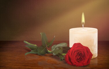 The concept of remembrance, funerals, and condolences. Candle and red rose on the desk