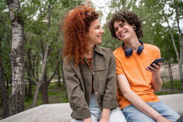 Fototapeta premium smiling man with smartphone talking to curly woman in park.