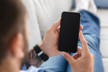Unrecognizable adult guy on couch, relax and look at smartphone with empty screen, at home