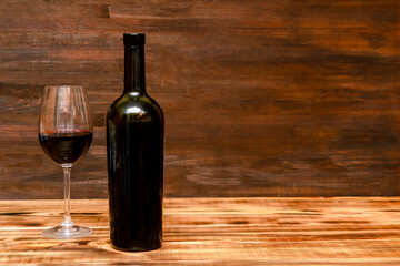 Red wine in glass, black bottle on wooden rustic table, alcohol drink, still life copy space, dark photo