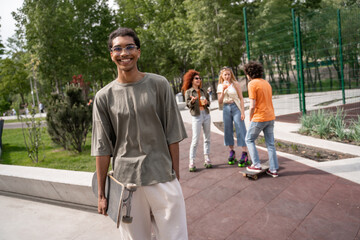 young and cheerful african american man holding skate near friends on background.
