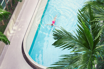 Vacation concept. Top view of slim young woman in red swimsuit swimming in the tropical pool.