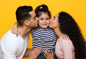 Fototapeta premium Parents Love. Happy Arab Mom And Dad Kissing Their Cute Little Daughter