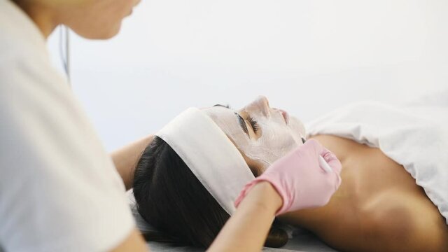Putting cream by using brush. Close up view of woman that lying down in spa salon and have face cleaning procedure