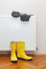 Photo of woolly hat, gloves and yellow wellies boots drying by radiator