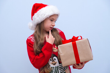 A girl with long hair in a red Santa hat is thoughtfully holding a box with a gift for Christmas and New Year in her hand. Place for advertising.
