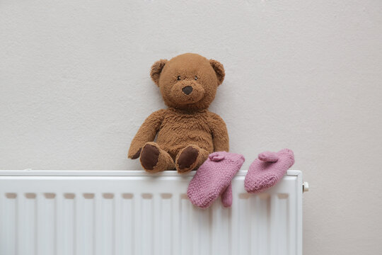 Photo of tedy bear and kid's woolen gloves drying on radiator. Winter season concept. 