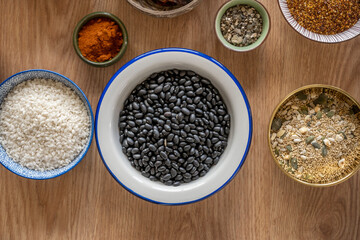 White bowl with black beans, next to it a bowl with rice, another with paprika and another with superfoods, quinoa and pumpkin and sunflower seeds