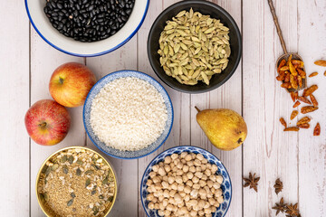 Bowls filled with uncooked rice, chickpeas, fragrant cardamom, black beans, cayenne on a spoon, pears and fresh red apples