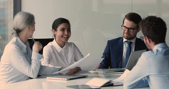 Multiethnic young and older businesspeople gather together discuss project, analyze financial stats do paperwork at meeting, employees brainstorm cooperating at briefing in boardroom, teamwork concept
