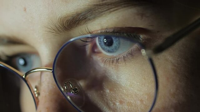 Close-up eyes of a teenage girl with glasses looks at the monitor, plays a game, reads, studies late at night