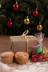 Christmas decoration details with a gift wrapped next to cupcakes and candies with chocolates, sweet food with Christmas tree with spheres in the background, studio and lifestyle