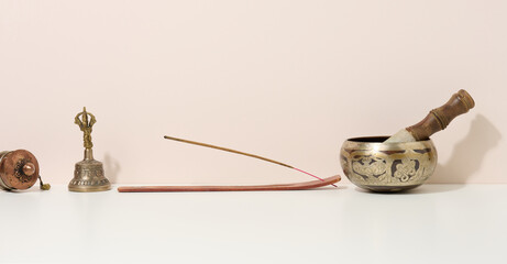 copper singing bowl and wooden clapper on a white table. Musical instrument for meditation,...
