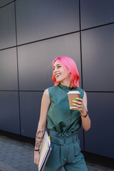 smiling businesswoman with pink hair and earphone holding coffee to go and folders.
