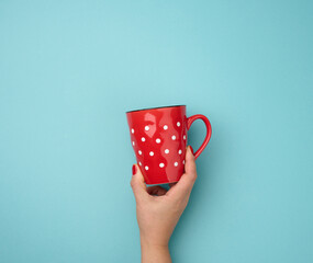female hand holding a red ceramic mug on a blue background, break time