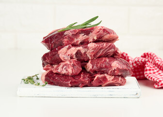 raw piece of beef ribeye with rosemary, thyme on a white table, close up