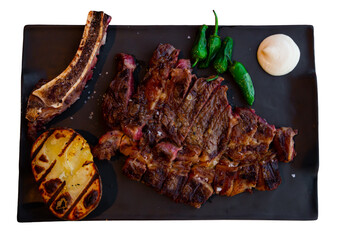 Sliced fried beef chop on bone served with creamy sauce and vegetable garnish of grilled potato and...