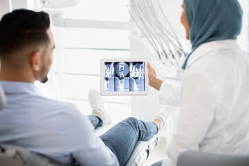 Fototapeta premium Muslim Female Dentist Showing Teeth X-ray On Digital Tablet To Male Patient