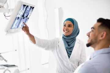 Obraz premium Islamic Dentist Lady Showing Teeth Xray On Digital Monitor To Male Patient