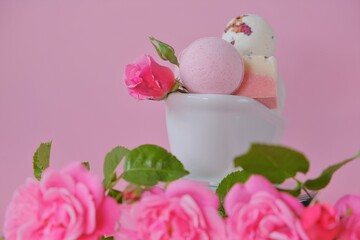Bath bombs with rose extract in a ceramic bath and pink roses on a pink background. Flower Bath Bombs.Organic vegan eco cosmetics. Beauty and aromatherapy.