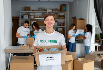Happy young male volunteer in uniform holding box for donation, team working together in charitable...
