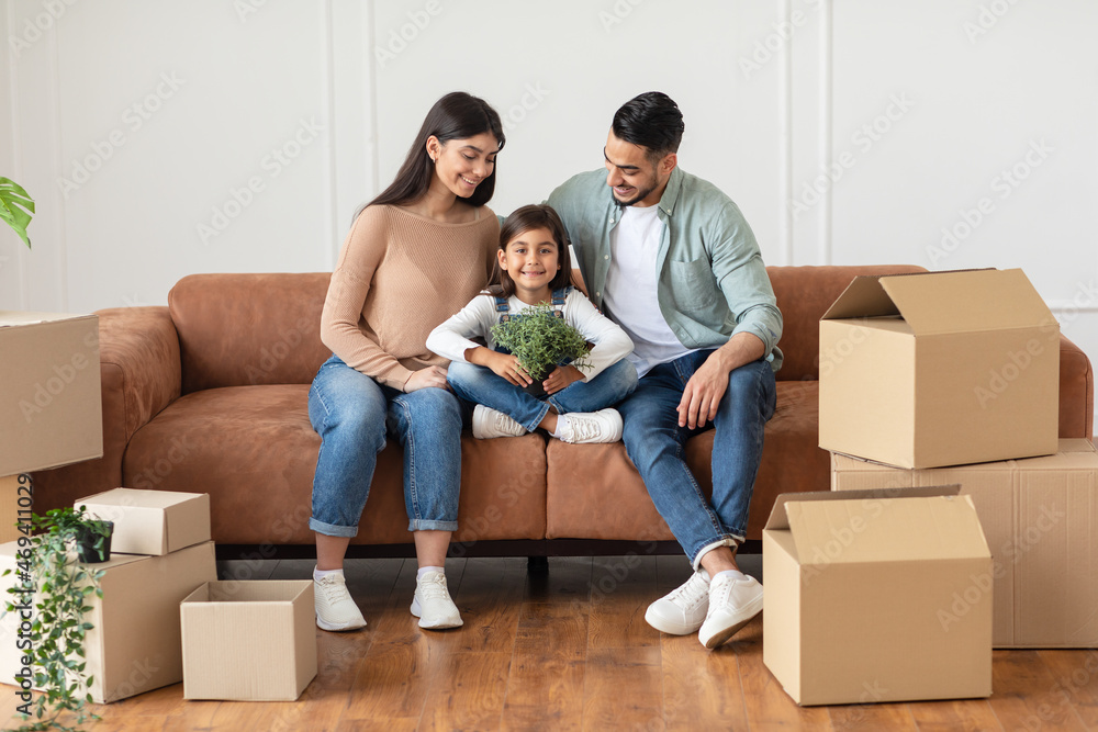 Poster positive young family sitting on sofa after relocation