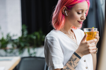 pleased businesswoman with pink hair and earphone holding cup of tea in office.