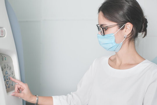 Woman Radiologist Doctor Adjusting Computer Tomography Scanner Machine To Make CT Test. Female Technician Wearing Face Mask Working In A Hospital Or Clinic For Covid-19 Patients.