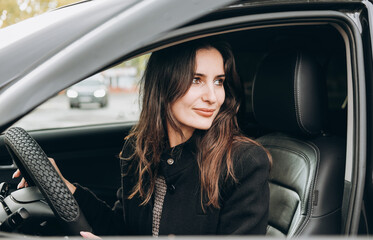 Obraz na płótnie Canvas young beautiful brunette woman sitting in a car and driving back. asian woman looking back smiling in a car