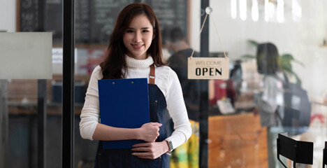 Portrait of a beautiful Asian woman in an apron standing in a coffee shop, she owns a coffee shop, the concept of a food and beverage business. Store management by a business woman.