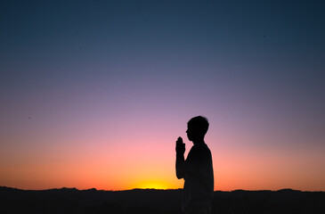 Fototapeta premium Silhouette of a man praying and thanking God with the sunset sky in the background. Concept of faith and spirituality.