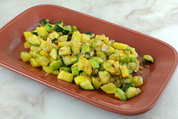 Sauteed chopped zucchini and crookneck yellow summer squash and shallot vegetable side dish on red...